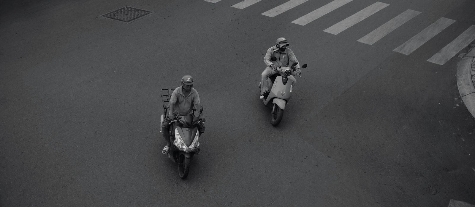 Two riders cross an empty road from above, each keeping to their own line